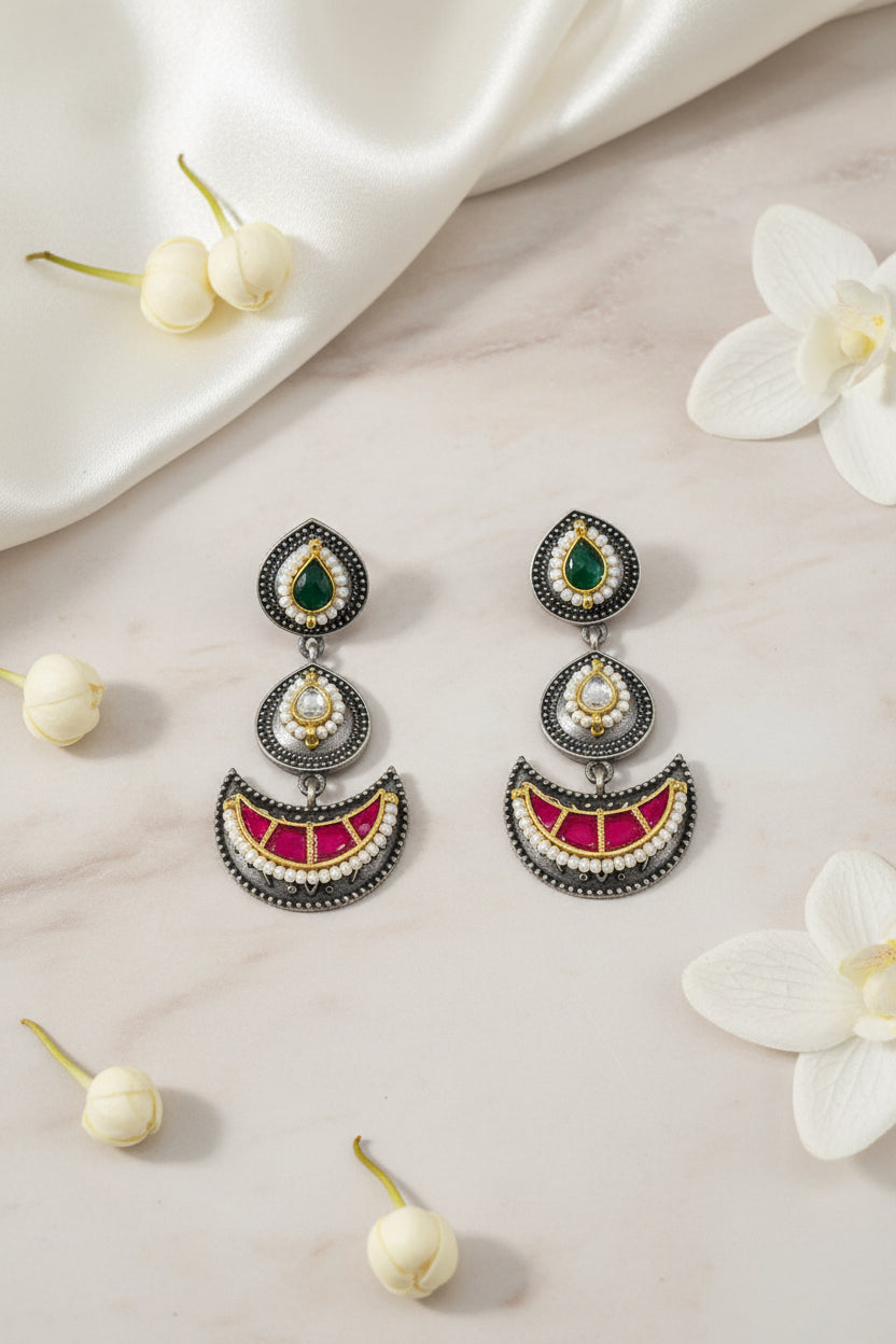 Ornate earrings with gemstones held between fingers against a dark green background