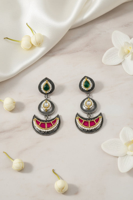 Ornate earrings with gemstones held between fingers against a dark green background