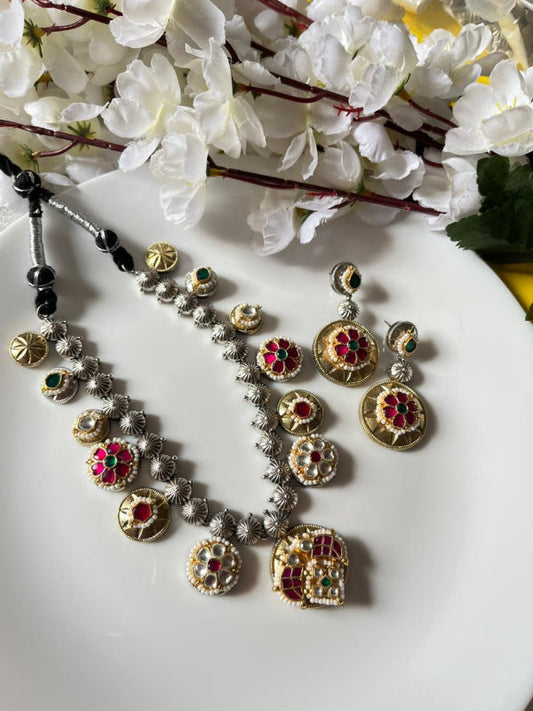 Silver necklace with colorful gemstones and matching earrings on a white plate with flowers in the background