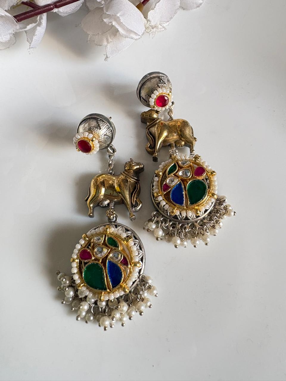 Ornate earrings with colorful gemstones and animal figures on a white background